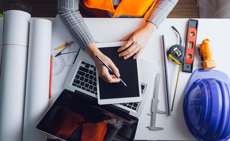 Zdjęcie dwóch kolegów omawia pracę z danymi i laptop typu tablet z włączonym projektem architektonicznym na budowie przy biurku w biurze