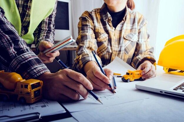 Dwóch kolegów omawia pracę z danymi i laptop typu tablet z włączonym projektem architektonicznym na budowie przy biurku w biurze