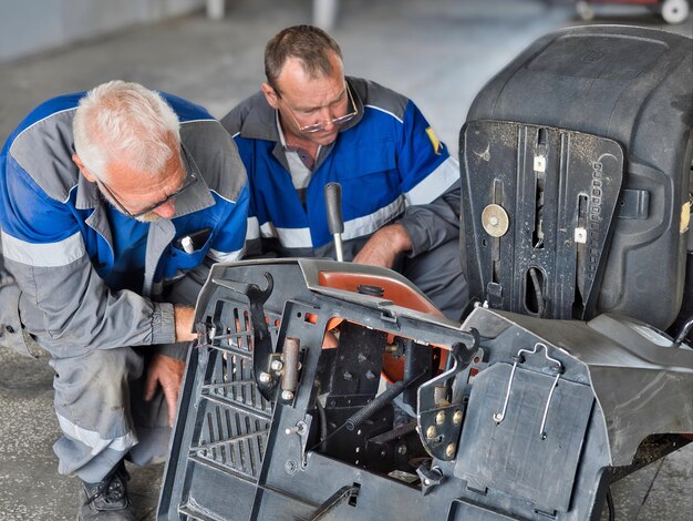 Zdjęcie dwóch mechaników naprawia urządzenia w garażu profesjonalni mechanicy samochodowi naprawiają traktory ogrodowe kosiarki trawnikowe w pomieszczeniach prawdziwy przepływ pracy