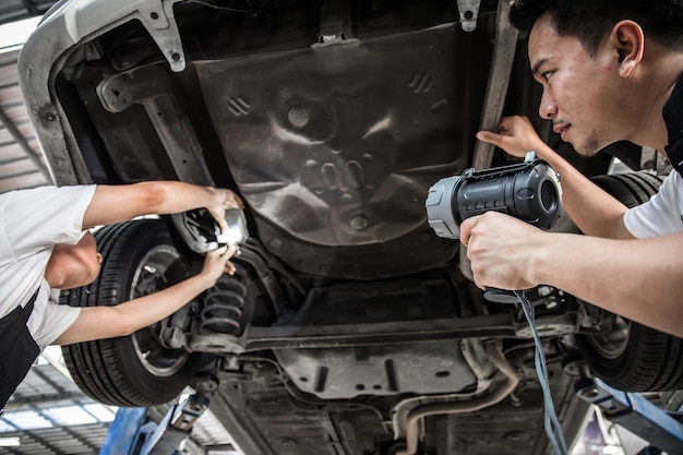 Dwóch mechaników sprawdzało zawieszenie auta. Pojazd podniesiony na podnośniku na stacji obsługi. Samochód w serwisie z naprawą dwóch osób. Mechanik samochodowy pracujący w serwisie samochodowym.