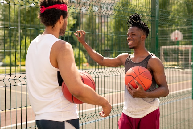 Dwóch młodych koszykarzy wielokulturowych wchodzących w interakcję po meczu, stojąc przy płocie