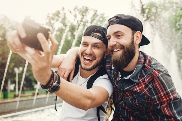 Dwóch młodych mężczyzn, uśmiechając się i bawiąc się w publicznym parku i biorąc selfie