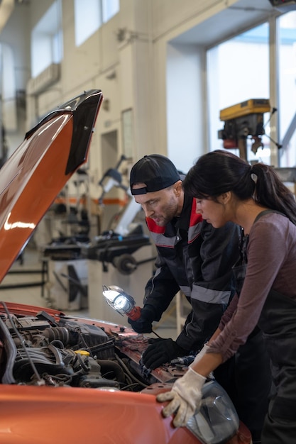 Dwóch młodych międzykulturowych mechaników w odzieży roboczej pochylającej się nad silnikiem Diesla