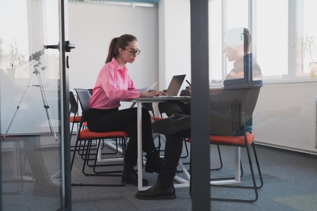 Zdjęcie dwóch młodych przedsiębiorców, biznesmen i bizneswoman, siedzących w nowoczesnym szklanym biurze i wymieniających się pomysłami biznesowymi.