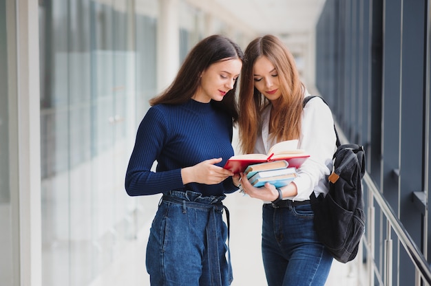 Dwóch młodych studentek stojących z książkami i torbami na korytarzu