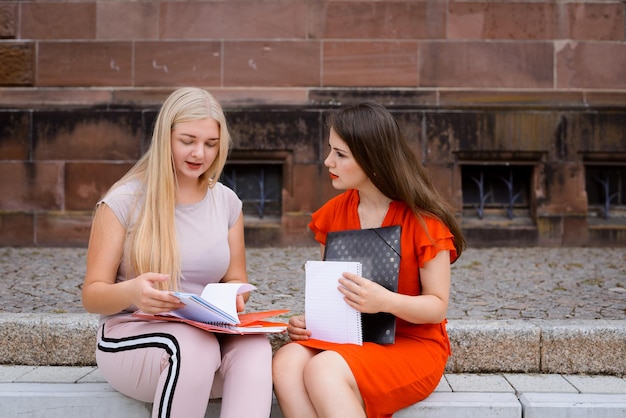 Dwóch najlepszych przyjaciół studentów pracujących z dokumentami, siedzących w pobliżu budynku uniwersytetu