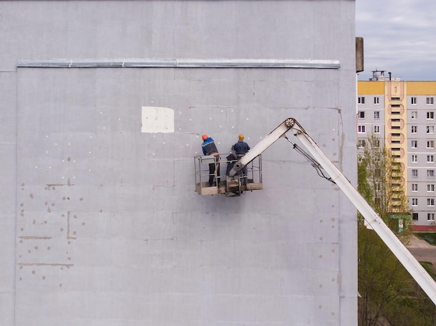 Dwóch pracowników stoi na podnośniku i izoluje ścianę domu