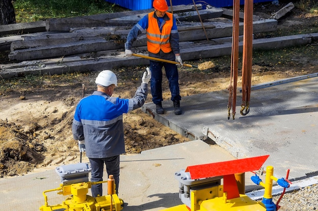 Zdjęcie dwóch pracowników w kaskach budowlanych i kombinezonach układających płyty betonowe na placu budowy w letni dzień budowniczowie wykonawców nadzorują układanie fundamentów na placu budowy autentyczny przepływ pracy