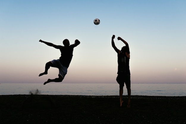 Dwóch przyjaciół grających w piłkę nożną na plaży.