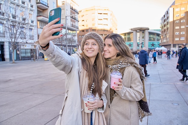 Dwóch przyjaciół robi sobie selfie z telefonem komórkowym w mieście z koktajlem w ręku kilka kobiet korzystających z zajęć rekreacyjnych