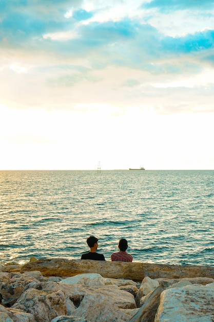 Dwóch przyjaciół rozmawia siedząc na skale i oglądając zachód słońca na plaży