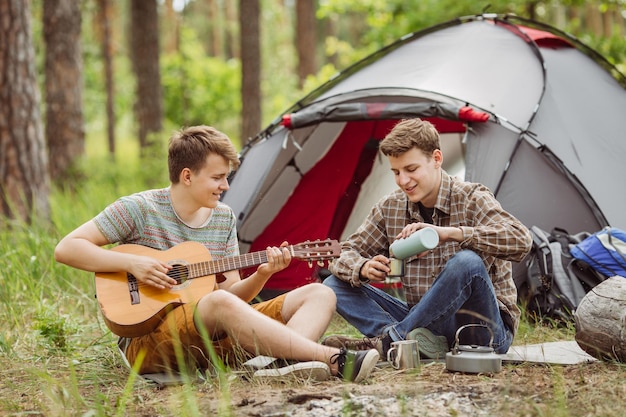 Dwóch przyjaciół siedzących w namiocie gra na gitarze i śpiewa piosenki