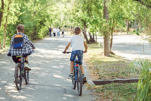 Zdjęcie dwóch radosnych chłopców jeżdżących rowerami po ścieżce rowerowej w parku z bujnym liściem w ciepły letni dzień