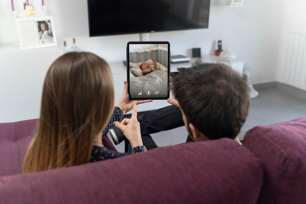 Dwóch rodziców siedzących na kanapie i monitorujących swoje dziecko na tabletie
