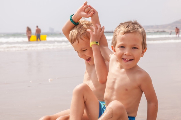 Dwóch ślicznych uroczych młodszych braci chłopców siedzi na plaży oceanu morza