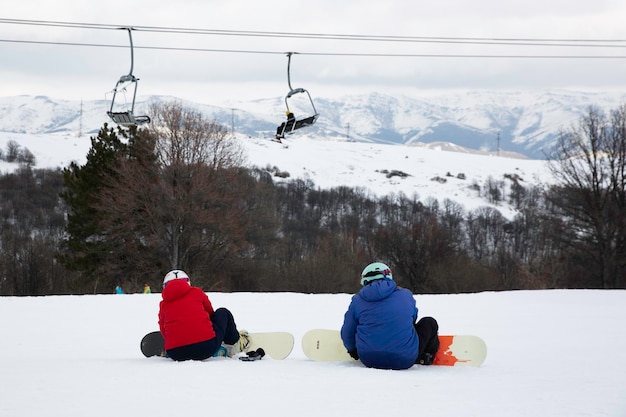 Zdjęcie dwóch snowboardzistów siedzących na śnieżnym zboczu