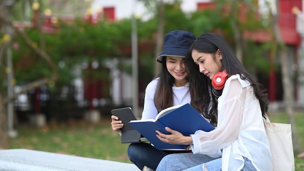 Dwóch studentów czytających książkę i rozmawiających ze sobą w kampusie.