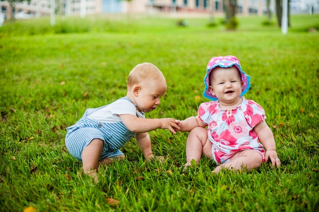 Dwóch szczęśliwych chłopców i dziewczynka w wieku 9 miesięcy, siedzących na trawie i wchodzących w interakcje, rozmawiających, patrzących na siebie.