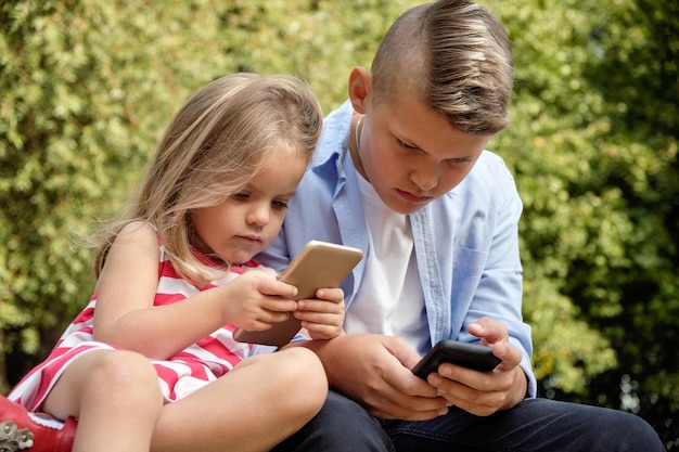 Dwóch szczęśliwych nastoletnich przyjaciół korzystających z telefonu komórkowego podczas relaksu w parku Problemy współczesnych sieci społecznościowych młodzieży w Internecie