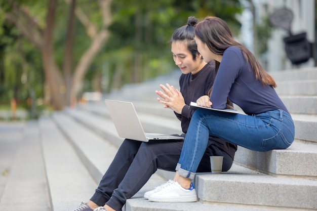 Dwóch szczęśliwych nastoletnich studentów studiujących pracę domową z zeszytu, siedząc na schodach na zewnątrz.