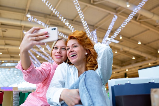 Dwóch szczęśliwych przyjaciół bierze selfie podczas zakupów w centrum handlowym.