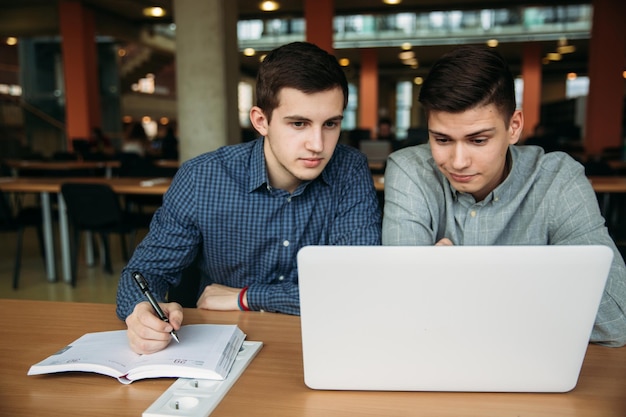 Dwóch uczniów korzysta z laptopa w bibliotece