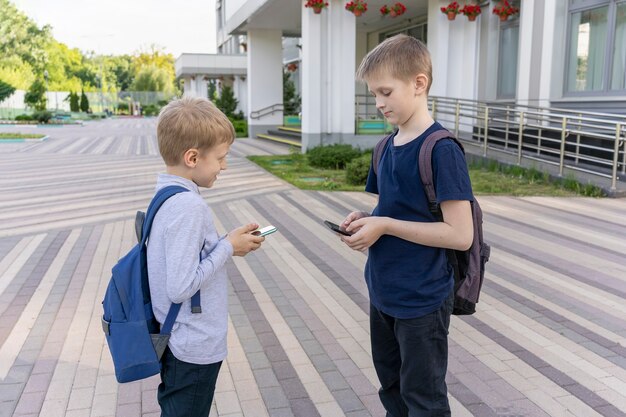 Dwóch Uczniów Z Plecakami Stoi W Tle Szkoły I Rozmawia Ze Sobą Przez Telefon