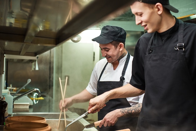 dwóch uśmiechniętych młodych asystentów szefa kuchni pracuje w kuchni restauracji