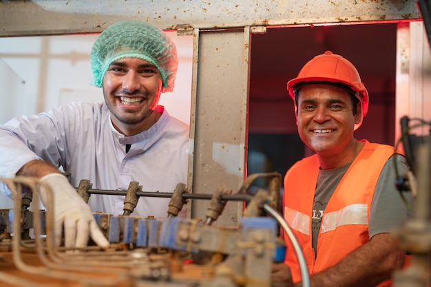 Dwóch uśmiechniętych starszych i młodych inżynierów pracujących w przemyśle fabryk żywności i napojów na linii produkcyjnej