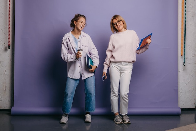 Zdjęcie dwóch uśmiechniętych studentów stojących z książkami próbuje pozować w studio na fioletowym tle z powrotem do ...