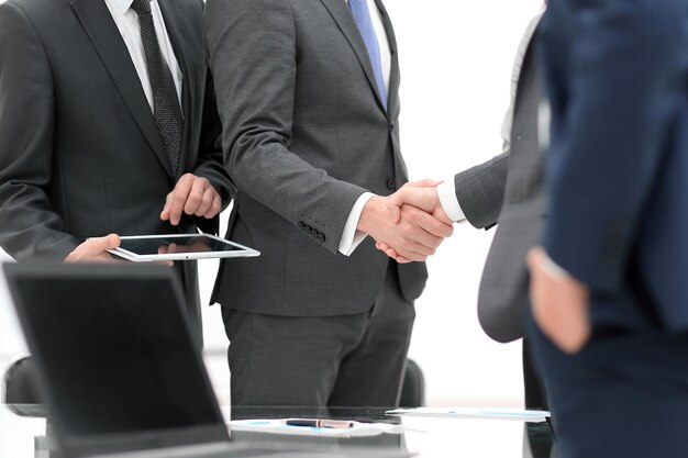 Dwóch wesołych biznesmenów, którzy z uśmiechem podają sobie ręce w biurze ze swoimi współpracownikami