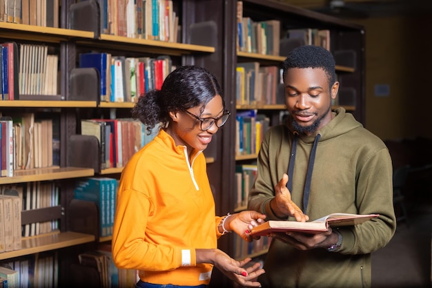 Dwóch wesołych studentów czytających razem książkę w bibliotece