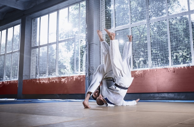 Dwóch zawodników judo wykazujących się umiejętnościami technicznymi podczas uprawiania sztuk walki w klubie walki. Dwaj wysportowani mężczyźni w mundurach. walka, karate, trening, sztuka, sportowiec, koncepcja zawodów