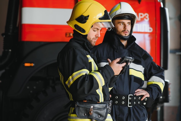 Dwóch Zawodowych Strażaków W Mundurach I Hełmach Ochronnych Pozuje Przed Wozem Strażackim