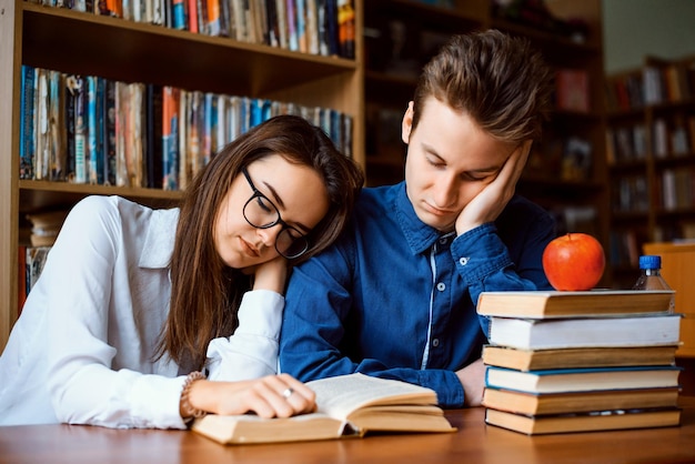 Dwóch znudzonych studentów w bibliotece Studentki i studentki czują się chore i zmęczone przygotowaniami do matury, czytając ostatnio wiele książek