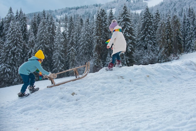 Dwoje dzieci na sankach z górskim zimowym dniem. Małe dzieci bawiące się na świeżym powietrzu na śniegu.