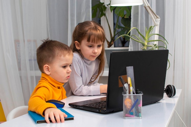 Dwoje dzieci patrzy na laptopa. Dzieci wpatrują się w laptopa.