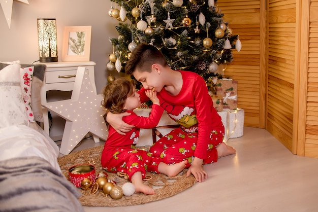 Dwoje dzieci siedzi na Boże Narodzenie przy choince i trzyma w rękach prezenty