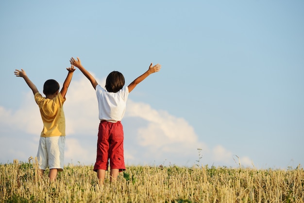 Dwoje dzieci stojących na łące z rękami w powietrzu