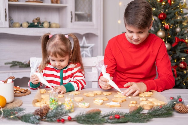 dwoje dzieci w piżamie gotuje świąteczne pierniki w świątecznej kuchni