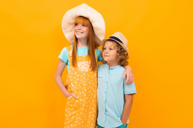 Dwoje rudowłosych dzieci w letnich kapeluszach na kolorowym żółtym