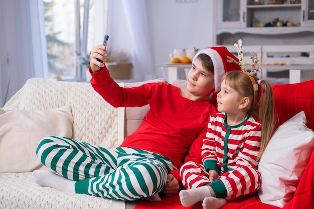 dwójka dzieci, chłopiec i dziewczynka w przytulnej świątecznej piżamie, rozmawiają przez telefon na czacie wideo z rodziną