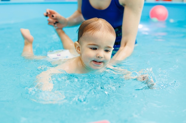Dwuletni chłopczyk uczy się pływać w basenie z trenerem Lekcje pływania dla dzieci
