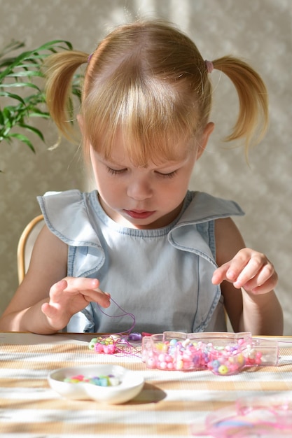 Zdjęcie dwuletnia dziewczynka siedzi i zbiera koraliki z małych koralików
