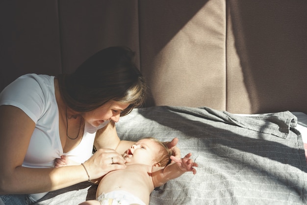 Zdjęcie dwumiesięczne dziecko bez ubrania, nagie, leżące w pieluszce na łóżku i uśmiechnięte do matki
