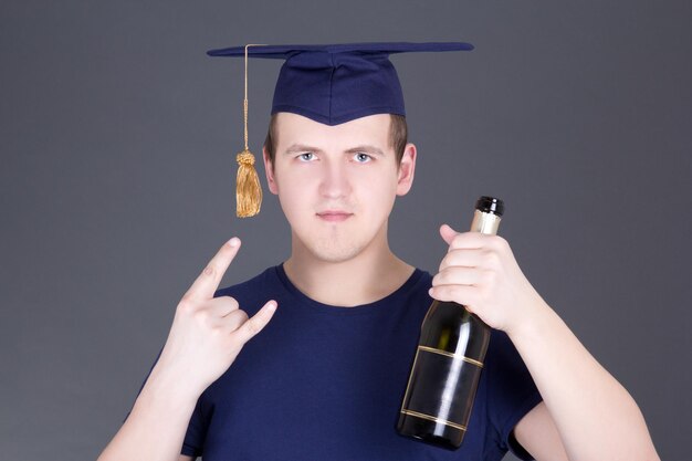 dyplomant z dyplomem i butelką alkoholu na szarym