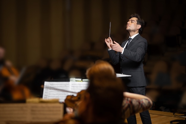 Dyrygent orkiestry symfonicznej z wykonawcami na tle sali koncertowej