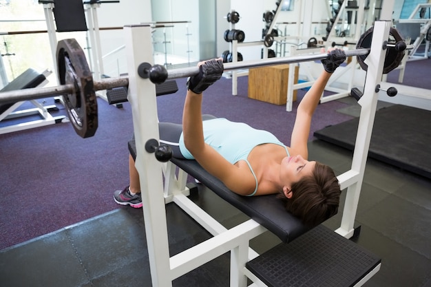 Dysponowana brunetka podnosi ciężkiego barbell lying on the beach na ławce