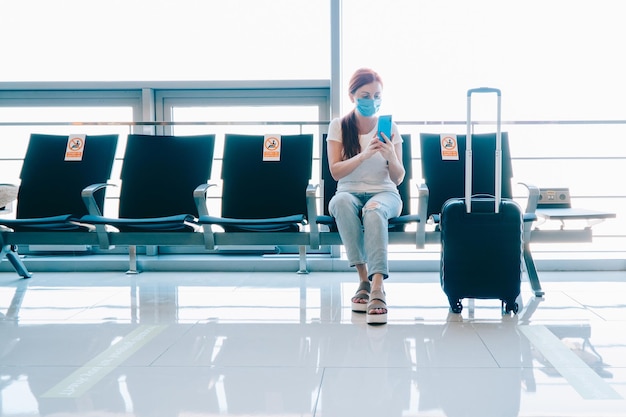 Dystans towarzyski Podróżująca kobieta korzysta ze smartfona w oczekiwaniu na lot w terminalu lotniska Naklejki na sąsiednich siedzeniach z napisem no sitting