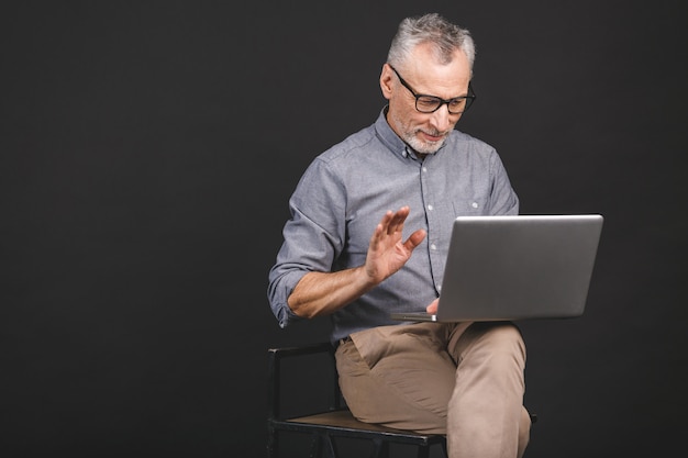 Dziadek korzystający z nowoczesnych technologii. Uśmiechnięty stary biznesmen w eyeglasses używać laptop